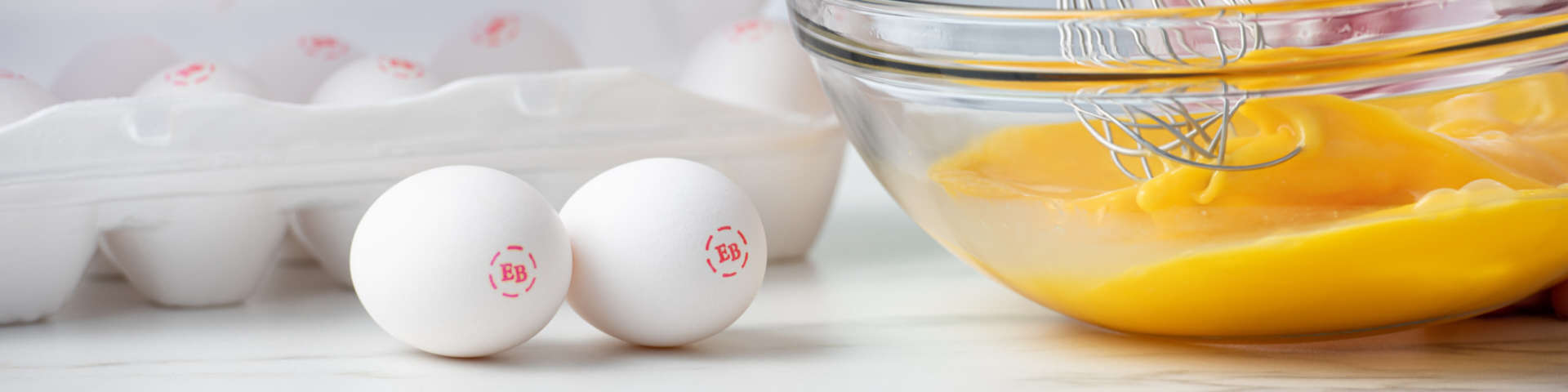 Two Eggland's best eggs next to a dish of eggs being scrambled.