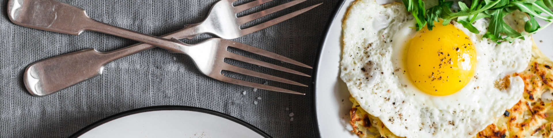 A sunny-side up egg on a dish on a table with two forks waiting to dig in!